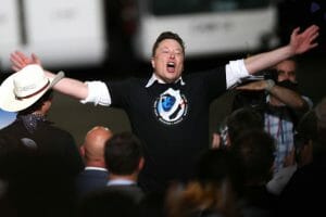 Tesla CEO Elon Musk is standing with his arms spread wide and his mouth wide open.