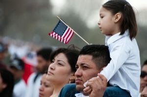 A young girl waving an American flag sits on a man's shoulders.