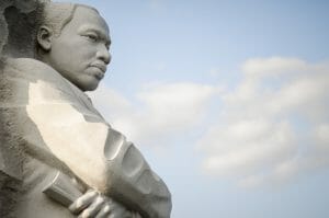 A statute of the Dr. Martin Luther King Jr. Memorial shown in profile in front of a sky blue background with clouds.