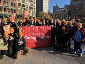A group of advocates in orange hats pose in NYC's Union Square with a large "Caring Majority" sign