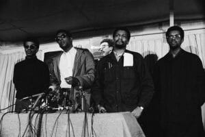 Black and white photo of four Black men standing at a dais.