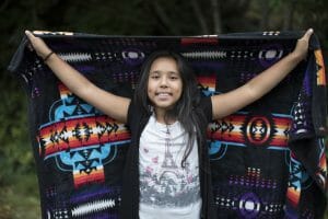A girl smiles at the camera holding a brightly colored blanket.