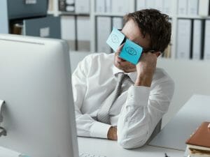 A person looking at a computer screen with pieces of paper taped in front of his eyes with eyeballs on them.