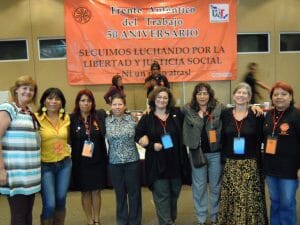 A group of women stand in front of a banner in Spanish about labor solidarity.