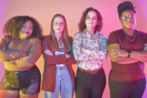 Four members of the Queer Food Foundation pose with arms crossed in front of a red and purple backgrop.