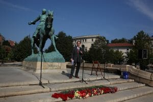 Man in a suit stands before a statute of a man on a horse.