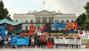 A group of climate activists stand in front of the White House with banners.