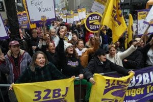 32BJ SEIU workers and allies rally in New York City with purple and yellow banners.